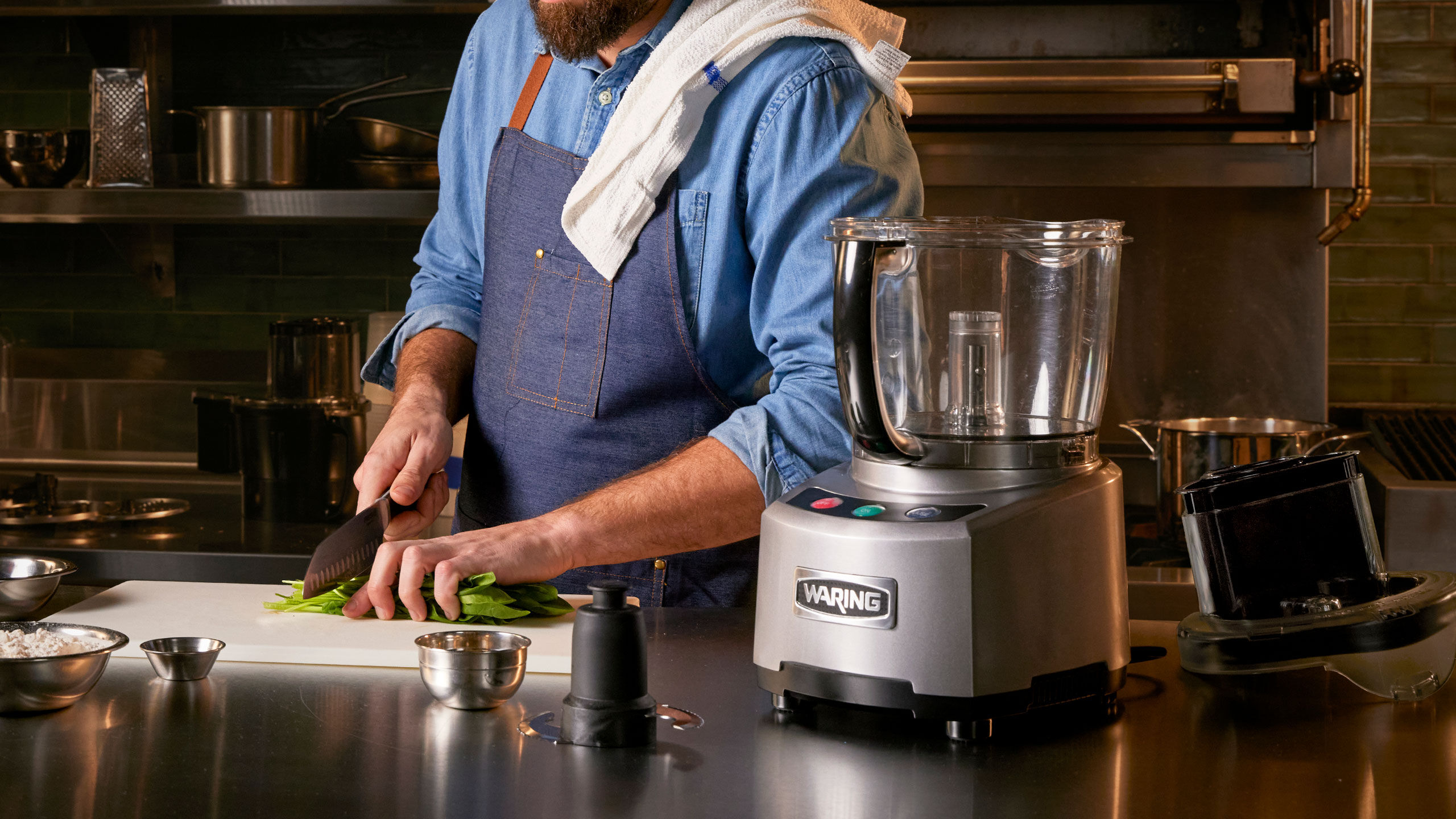 Chef chopping ingredients with a food processor on the counter beside him.