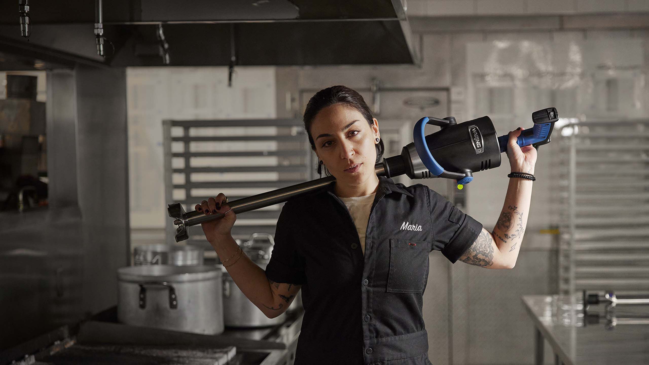 Female chef holding immersion blender across her shoulders.