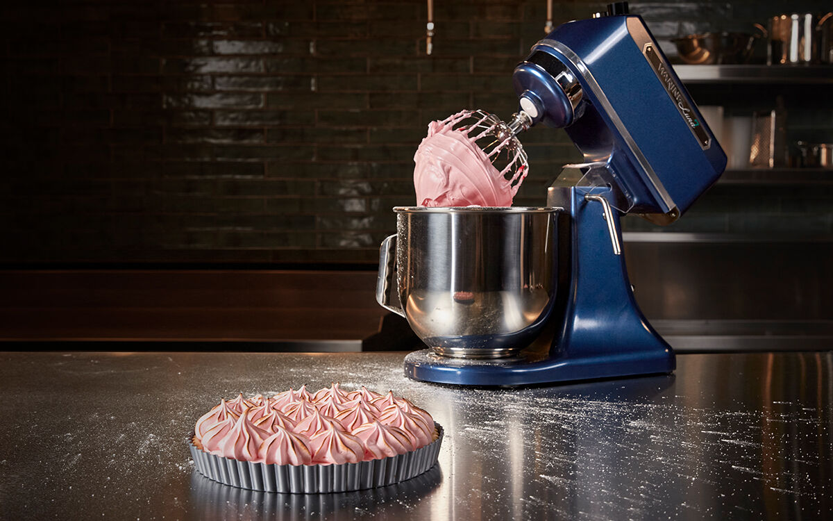 blue stand mixer on counter with pink meringue on whip and a meringue torte in front of it. 