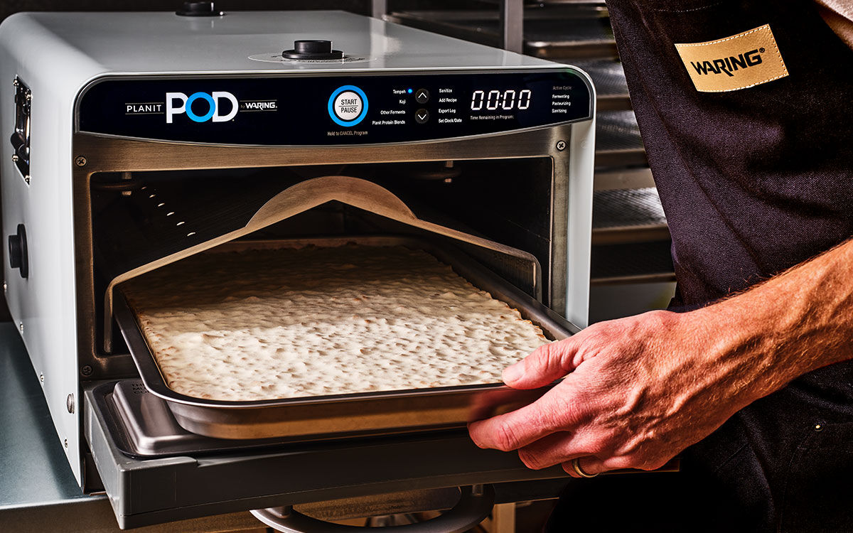 hand pulling a tray of tempeh out of the planit POD fermentation chamber